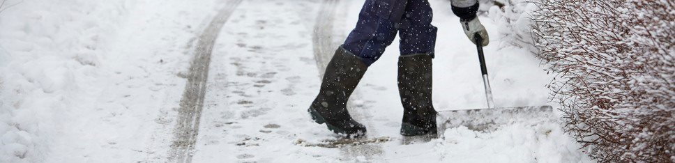 De stövelförsedda benen hos en man som skottar snö